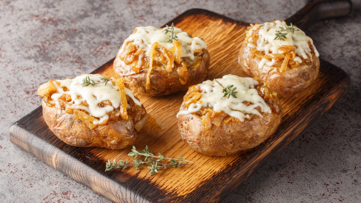 Vier French Onion Potatoes auf einem Holzbrett mit Thymianzweig und grauem Tisch. Alles von schräg oben fotografiert.