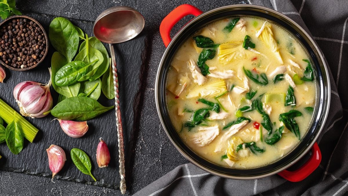 Hähnchensuppe mit Spinat und Artischocken in einem Topf. Daneben Suppenkelle und Zutaten.