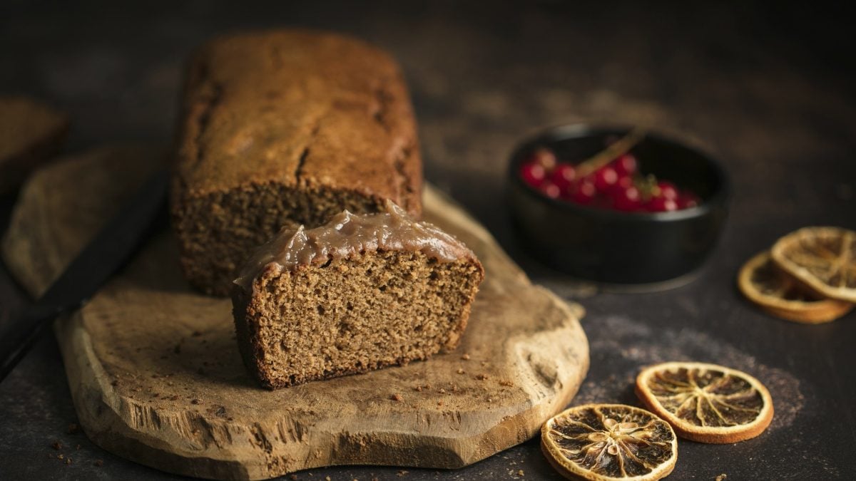 Der Kuchen auf einem Holzbrett und dunklem Untergrund. Daneben getrocknete Orangenscheibe und eine Schale mit roten Beeren.