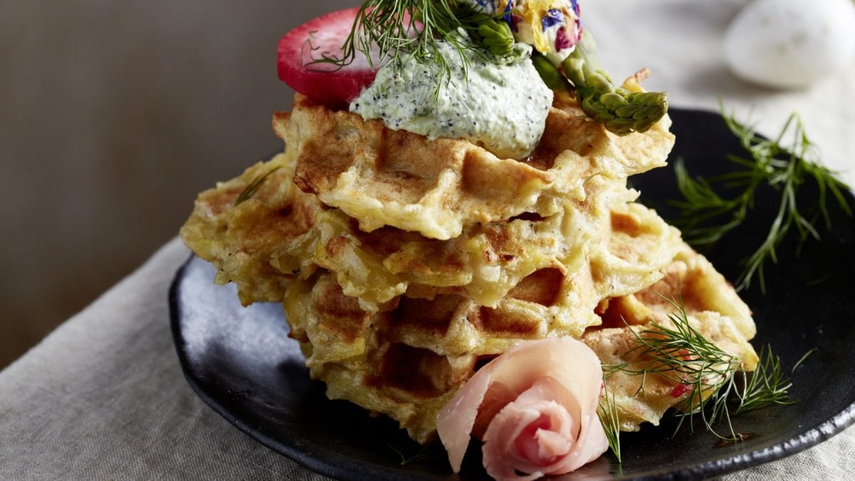 Knusprige Schmandwaffeln mit Antipasti auf einem schwarzen Teller auf einem beigen Hintergrund.