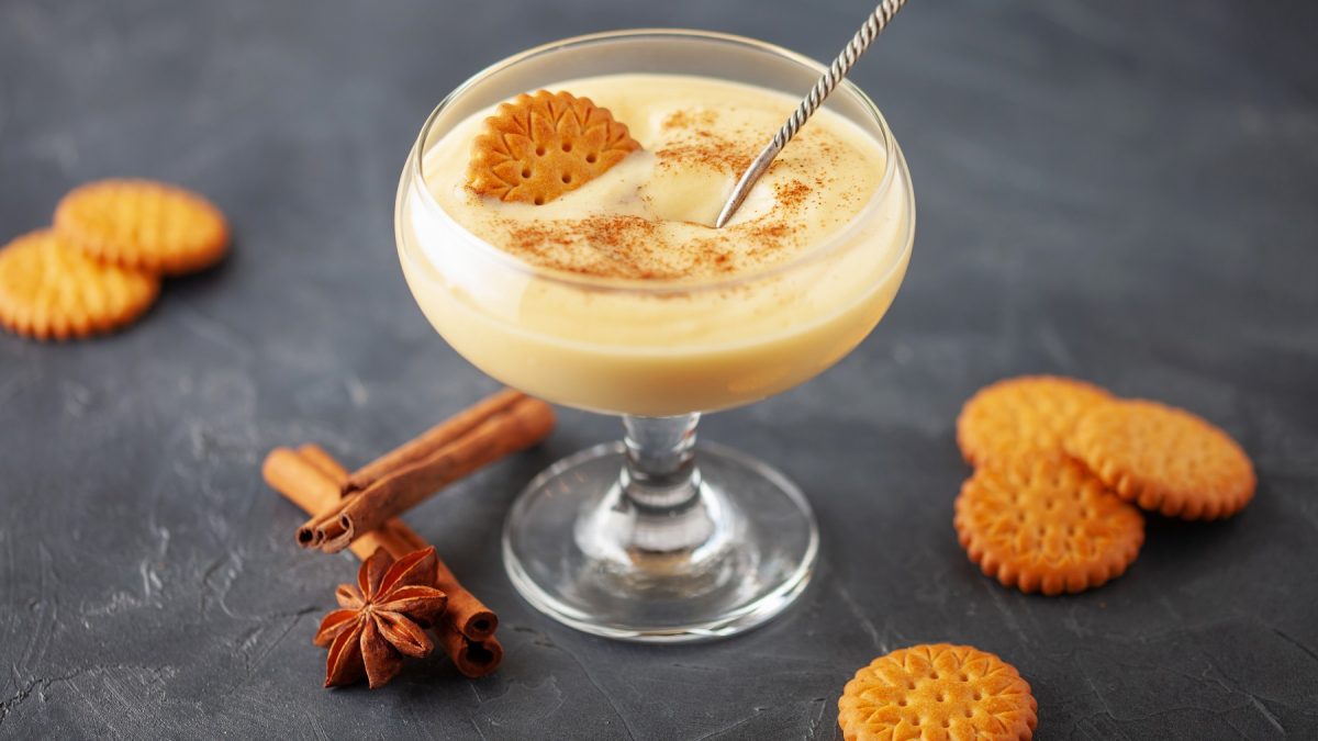 Natillas de vainilla in einer Glasschale mit runden Keksen, Zimtstange und Anisstern.