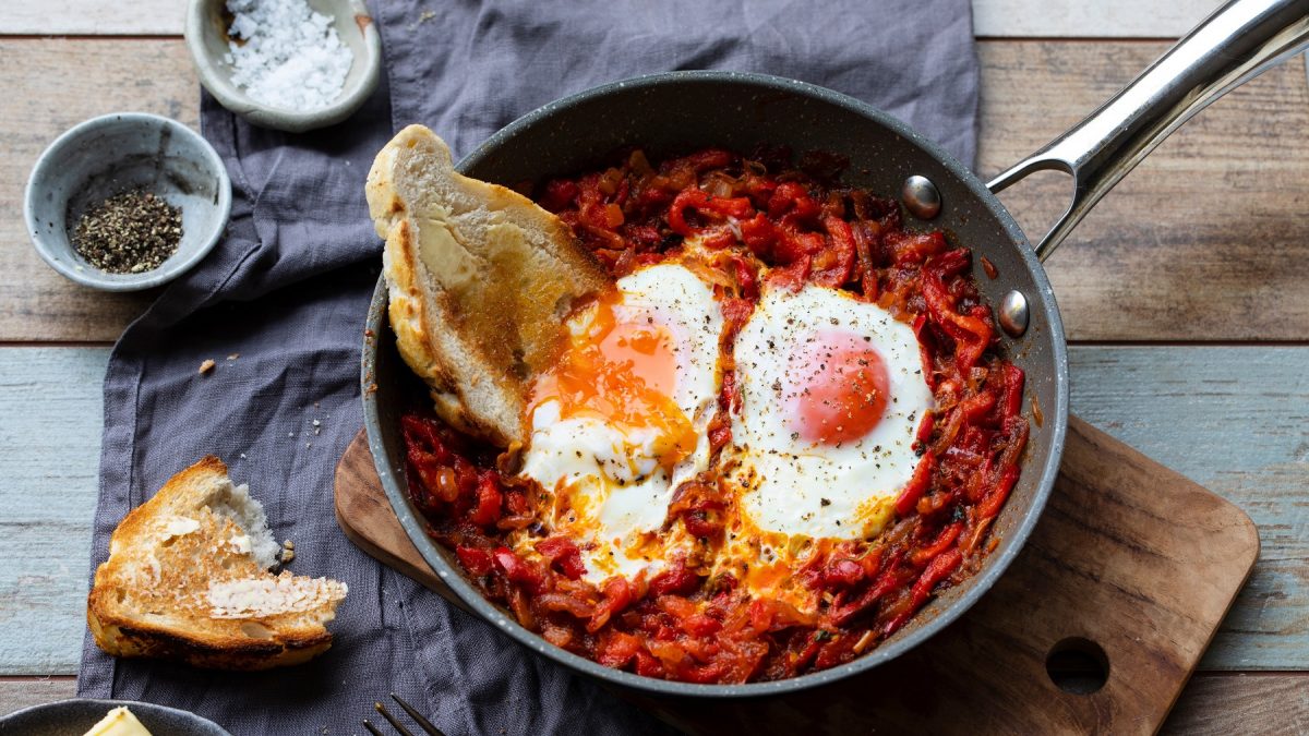 Paprikapfanne mit Nduja und zwei Eiern. Darin eine Scheibe Brot mit Butter. Von oben fotografiert.