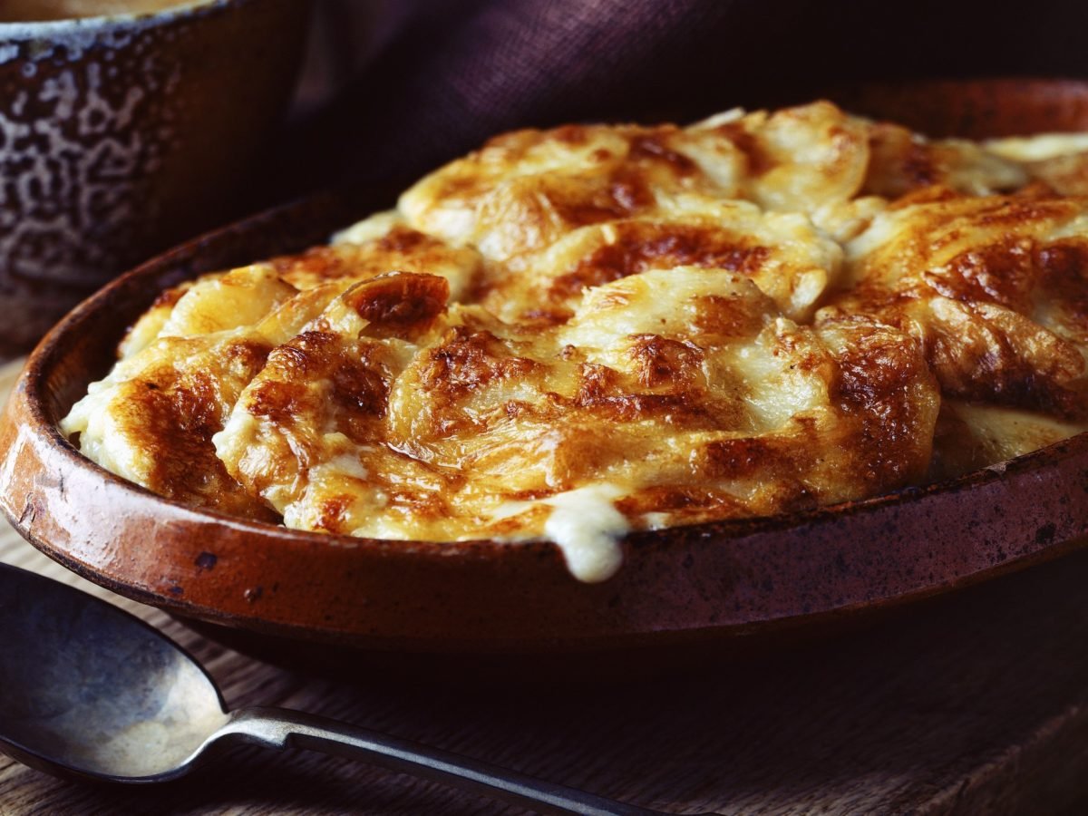 Auflauf mit Kartoffeln in einer Backform. Alles von der Seite auf einem dunklen Tisch fotografiert.