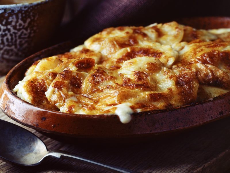 Auflauf mit Kartoffeln in einer Backform. Alles von der Seite auf einem dunklen Tisch fotografiert.