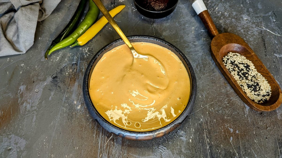 Eine graue Schale mit der koreanischen Chili-Mayonnaise auf einem Steintisch mit Sesam und Chilischoten. Alles von oben fotografiert.