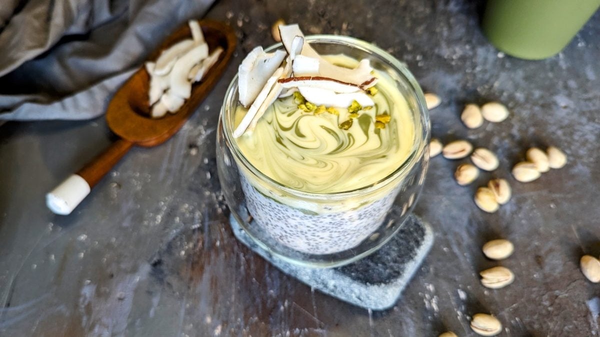 Das Glas mit der Kokos-Pistazien-Bowl auf einem Steintisch von schräg oben fotografiert.