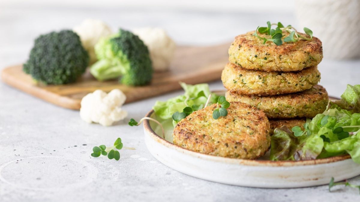 Quinoa-brokkoli-Burger auf einem Teller. Daneben Brokkoli und Blumenkohl.