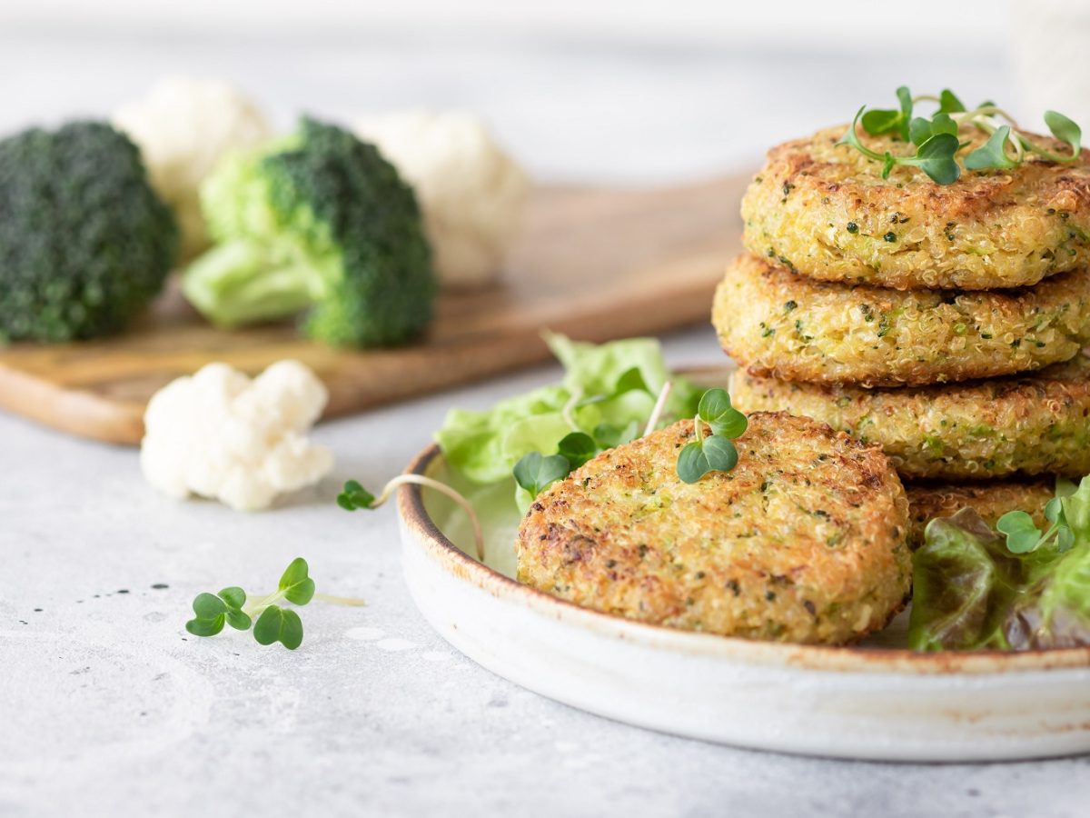Quinoa-brokkoli-Burger auf einem Teller. Daneben Brokkoli und Blumenkohl.