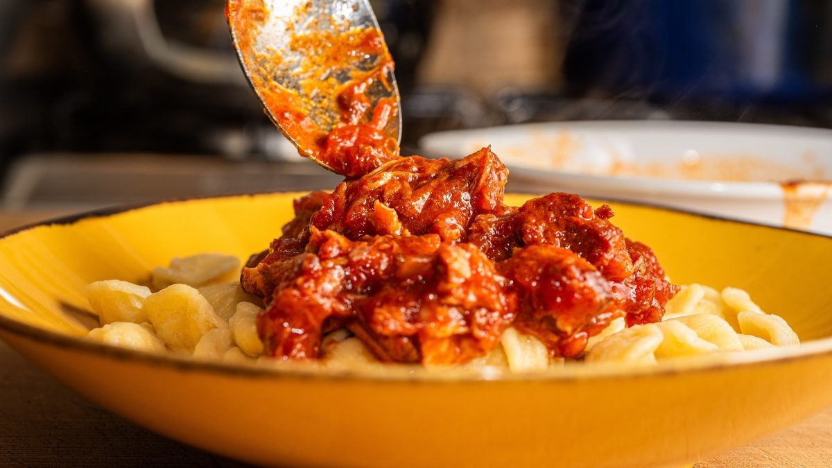 Ragù napoletano, dass mit einem Löffel auf Pasta auf einem gelben Teller gegeben wird.