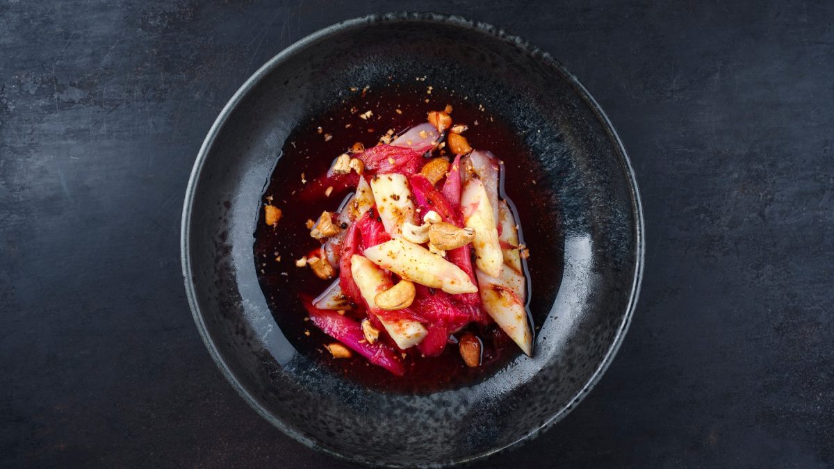 Spargelsalat mit Rhabarber-Vinaigrette und Cashewkernen auf einem schwarzen Teller.