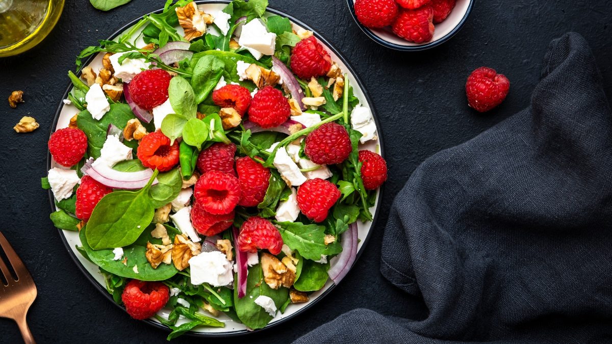 Spinat-Salat mit Himbeeren, Ziegenkäse, Walnüssen und roten Zwiebeln auf einem Teller.