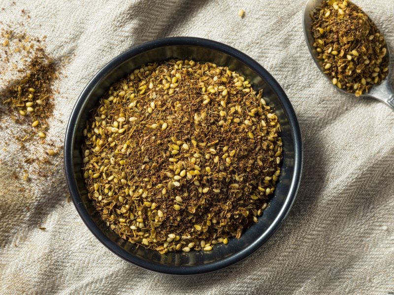 Nahaufnahme von Zaatar-Gewürz in einer schwarzen Schale und einem Löffel auf Leinenstoff.