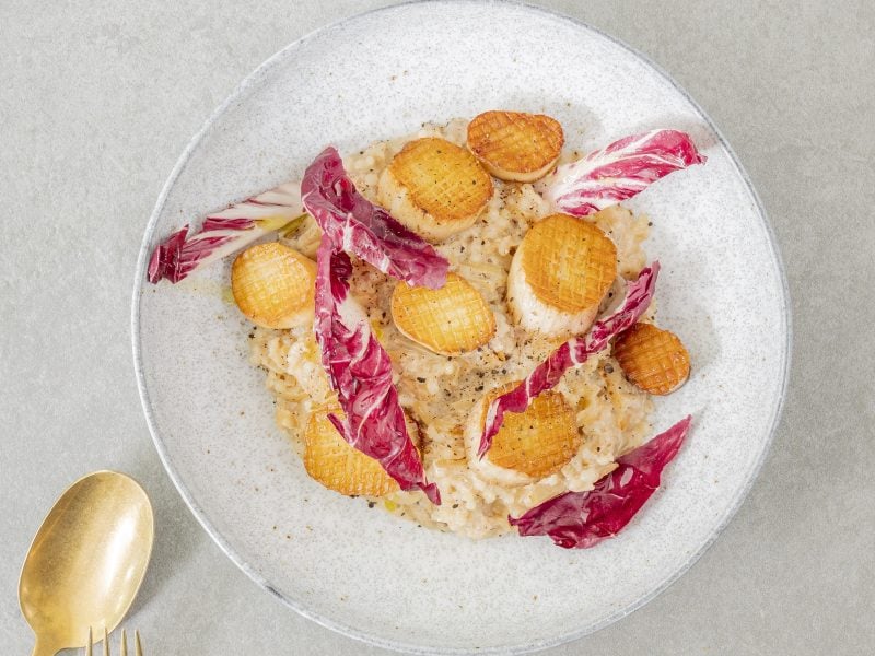 Ein weißer Teller mit den Kräuterseitling-Scallops auf beigem Untergrund direkt von oben fotografiert. Daneben noch ein goldener Löffel erkennbar.