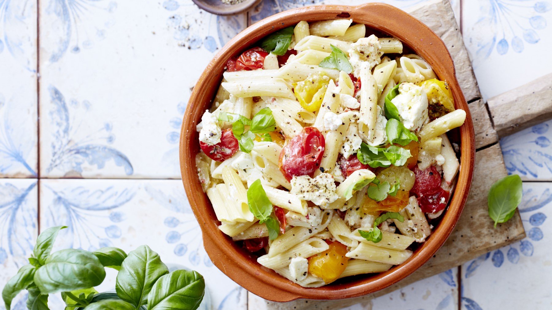 Baked Feta Pasta mit frischen Basilikum in runder Ofenform auf hellem Untergrund.