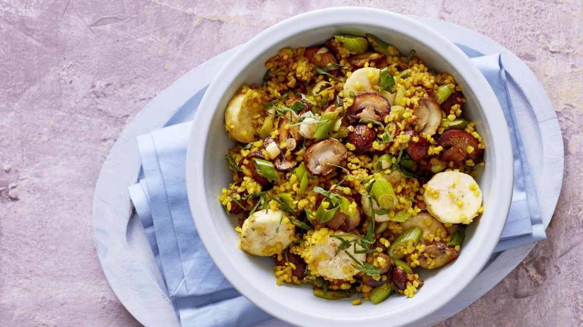 Ausgefallene Gemüsepfanne mit Banane und Bulgur auf Teller vor pinkem Untergrund