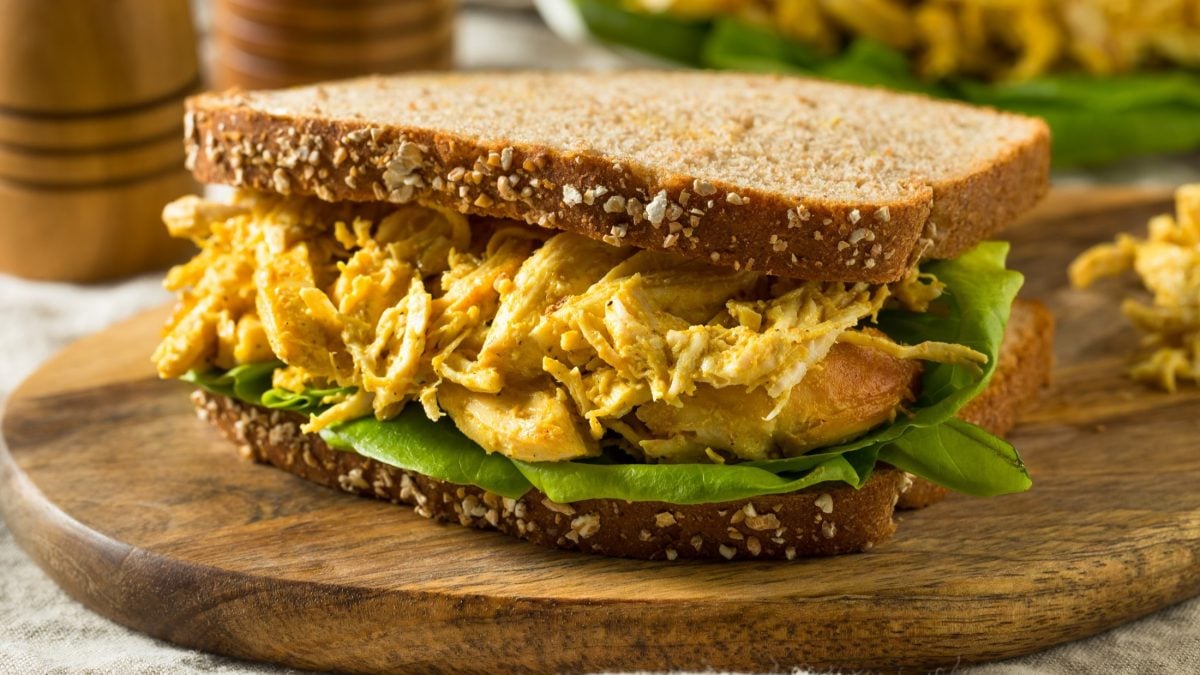 Frontal: Ein Coronation-Chicken-Sandwich auf einem Holzbrettchen.
