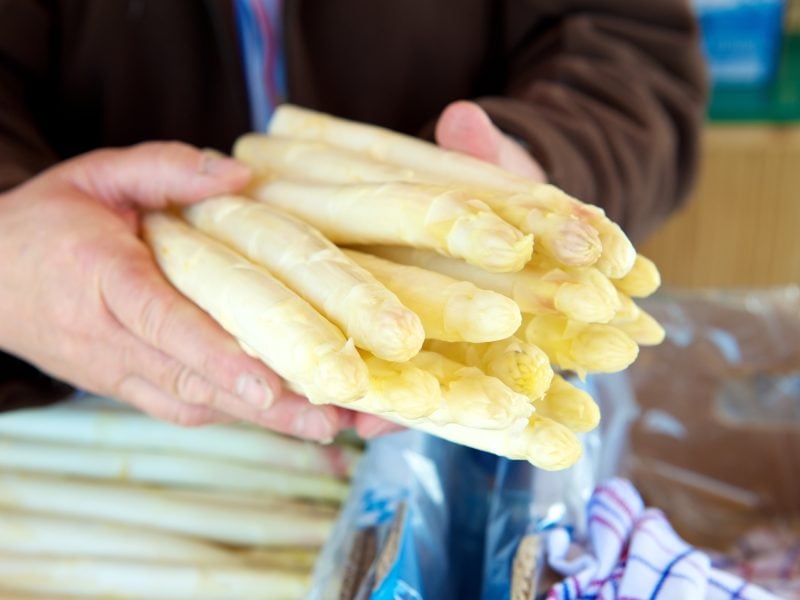 zwei männliche Hände haten frischen frischen Spargel. / Eine Kiste mit frischem Spargel