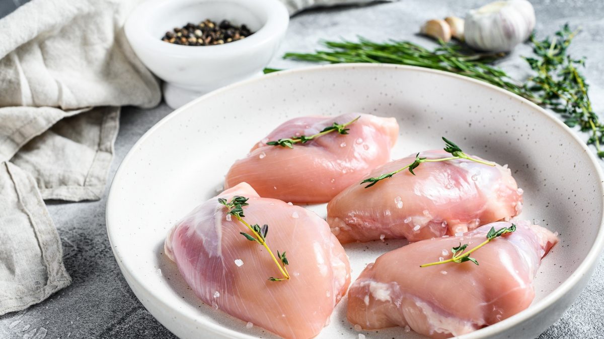 Draufsicht schräg: Auf einem Tisch liegt eine helle, runde Schale. In der liegen vier Hühnerfilets, die mit einem Thymianzweig und Salz belegt würden. / Hygiene-Regeln bei Geflügel