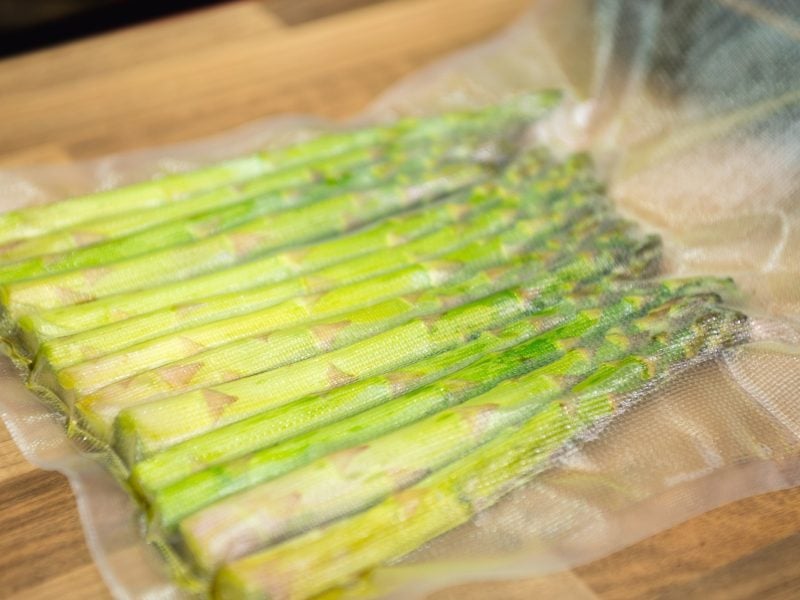 Vakuumierter Spargel auf einem Holzbrett und Steinuntergrund.