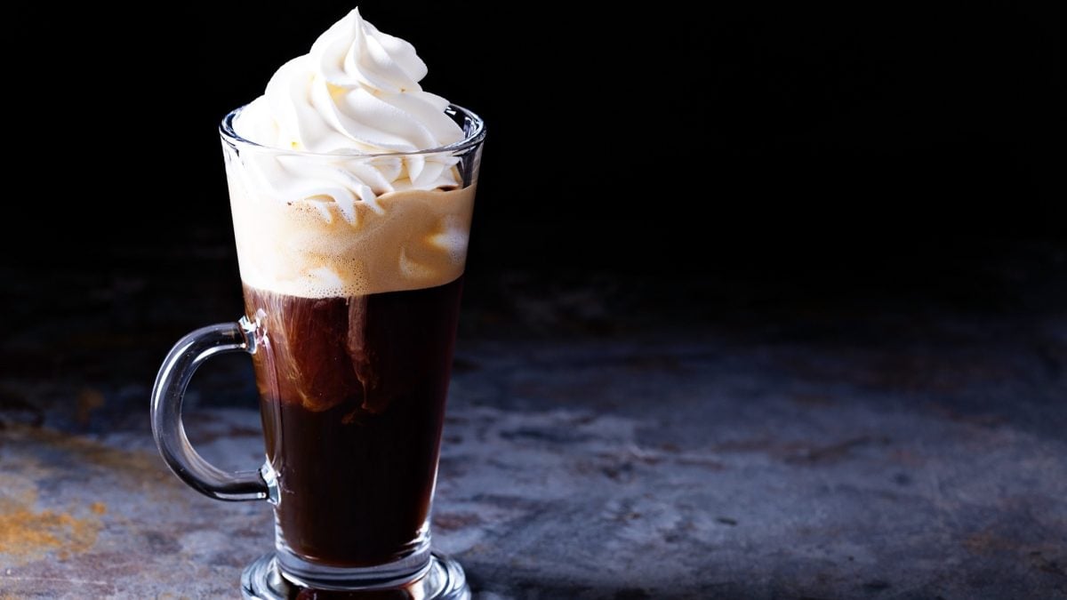 Frontal: Ein Glas Wiener Eiskaffee mit einer Sahnehaube steht auf einem Boden aus Holz.