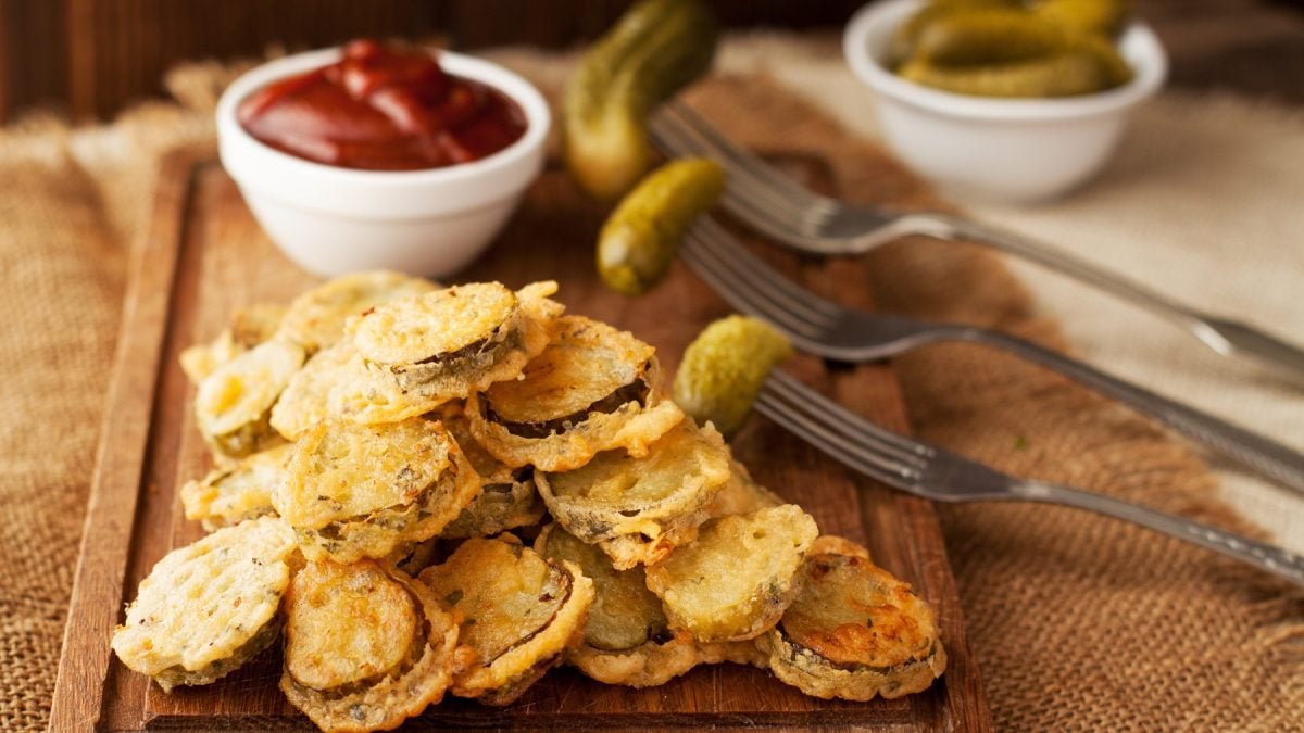 Fried Pickles im Vordergrund. Im Hintergrund Schale mit Ketchup und Essiggurken auf Gabeln.