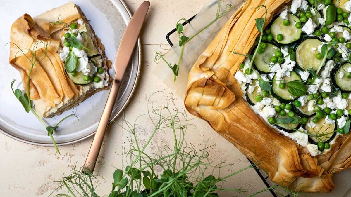 Frühlingstarte aus Filoteig mit Feta, Zucchini und Ebsen. Daneben ein Stück der Tarte auf einem Teller.
