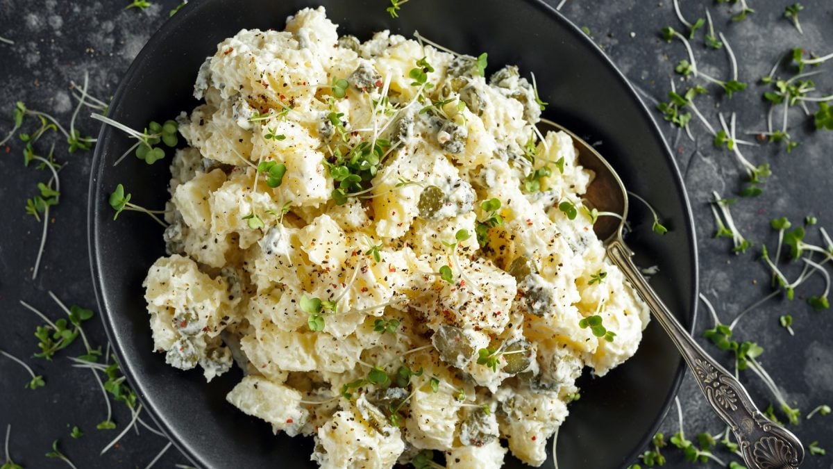 Schwarzer Teller mit cremigem Kartoffelsalat. Alles direkt von oben fotografiert.