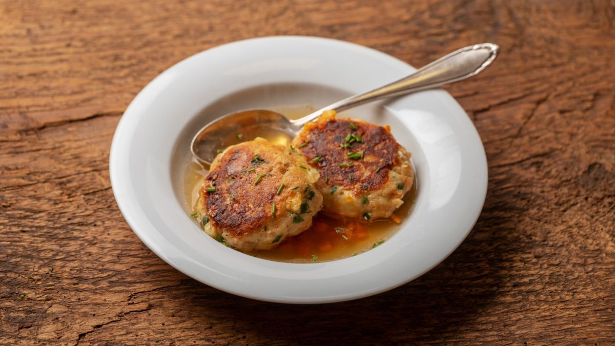 Kaspressknödel in einem weißen Suppenteller auf hölzernem Hintergrund.