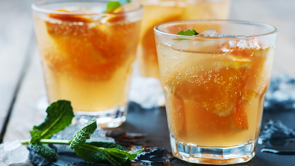 Drei Gläser auf einem Holztisch mit Minze und Orangen im Glas. Alles von der Seite fotografiert.
