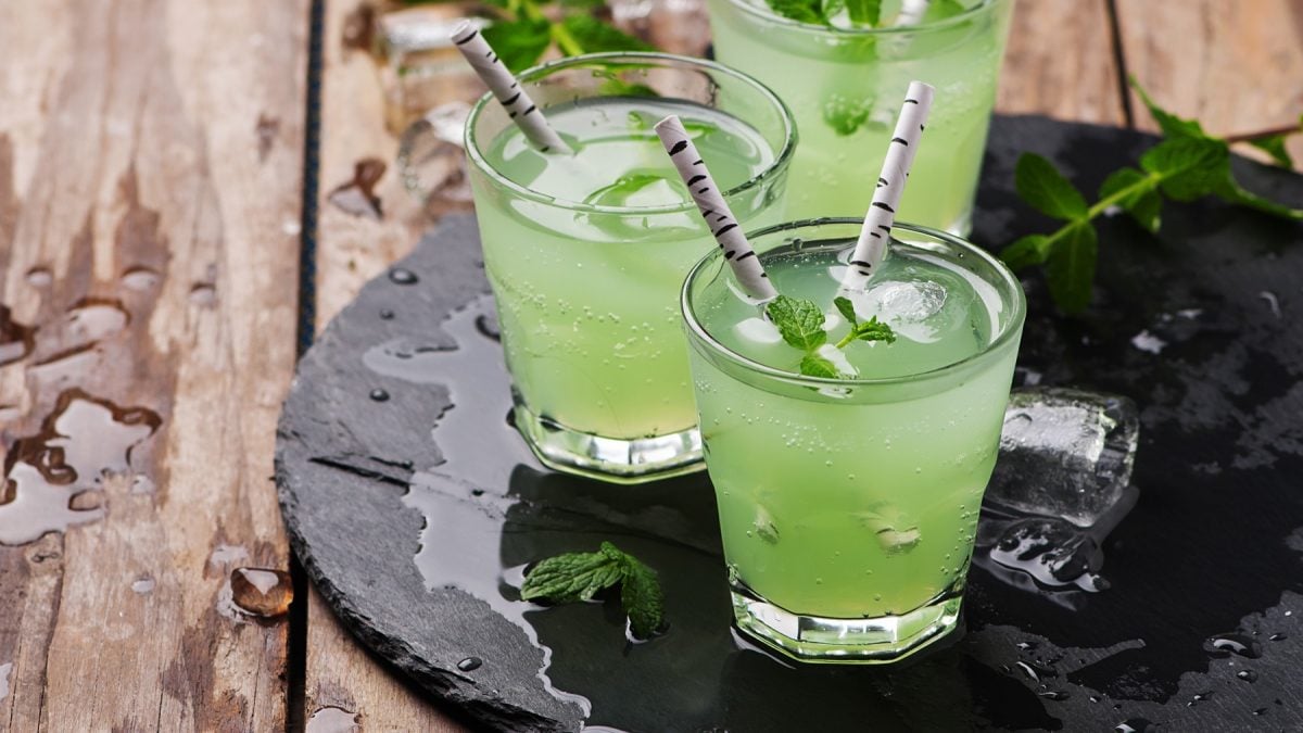 Drei Gläser mit dem grünen Drink auf einer schwarzen Schiefertafel und rustikalem Holztisch. Alles von der Seite fotografiert.