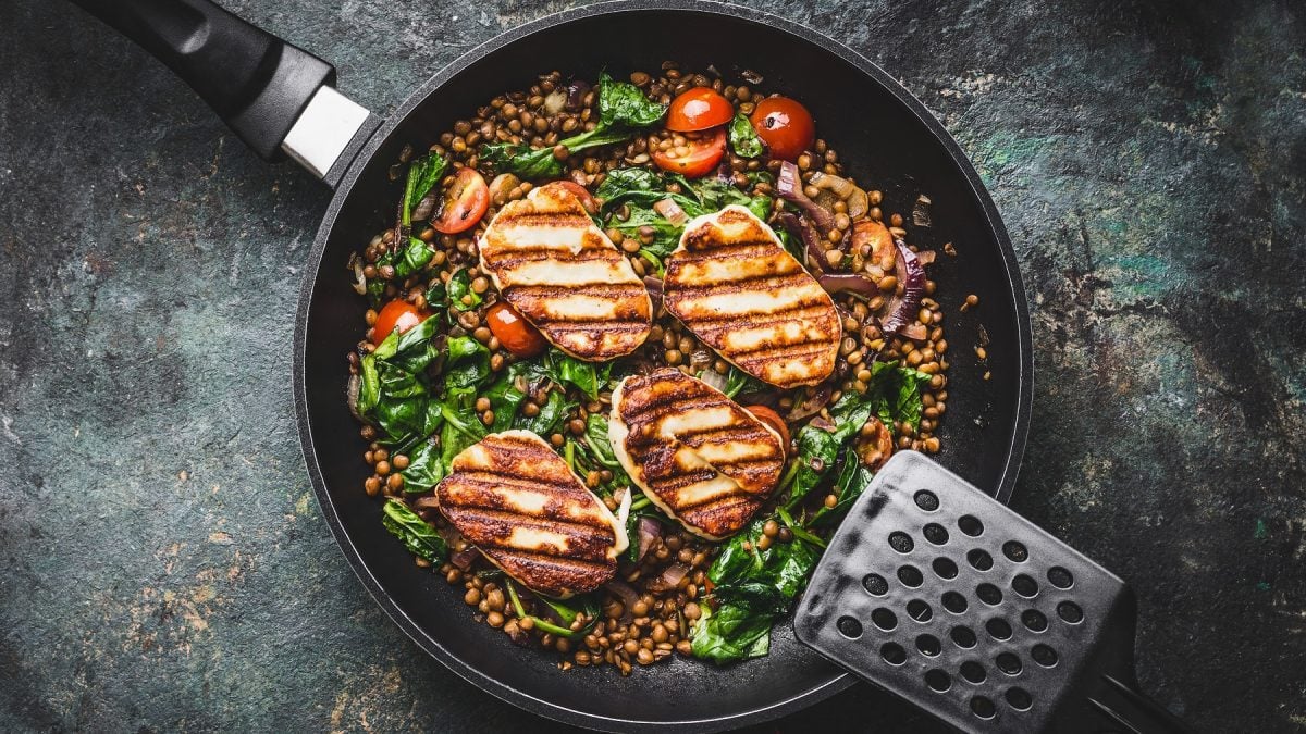 Linsen-Spinat-Gemüse mit Halloumi und Cherrytomaten in einer Pfanne von oben fotografiert.