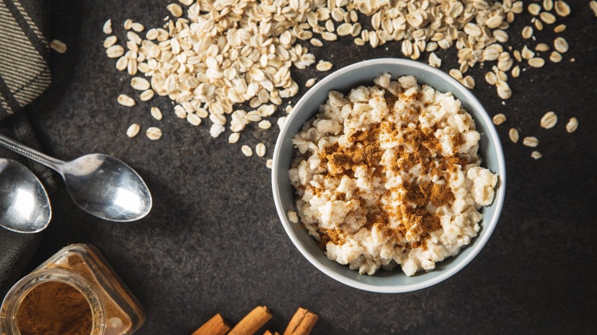 Porridge auf Basis eines Grundrezepts in einer weißen Schüssel mit Zimt. Daneben Löffel, Haferflocken und Zimtstangen.