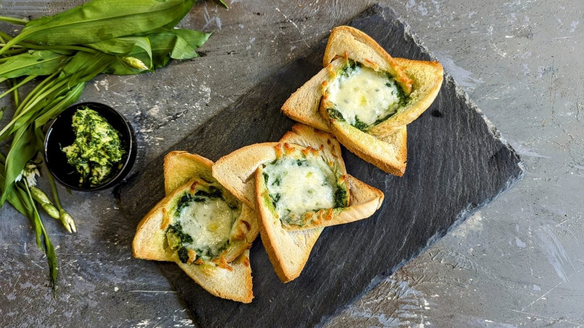 Drei Twisted Toasts mit Bärlauchbutter und Käse überbacken auf einer schwarzen Schieferplatte. Alles von oben fotografiert.