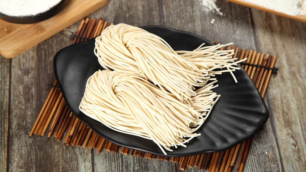 Selbstgemachte Ramen auf einem schwarzen Teller und Bambusmatte. Alles auf einem rustikalen Holztisch von schräg oben fotografiert.
