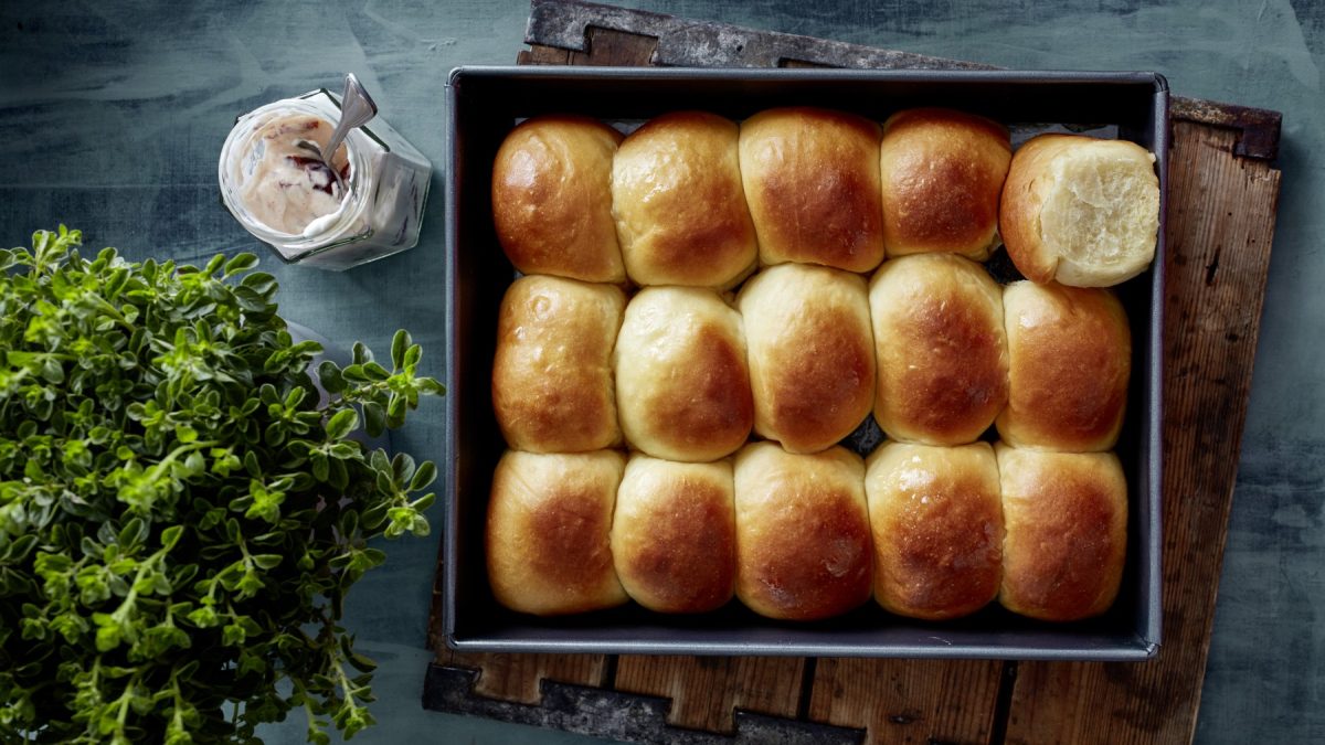 Hawaiian Buns in einer schwarzen Form auf dunkelblauem Hintergrund. Links eine Pflanze.