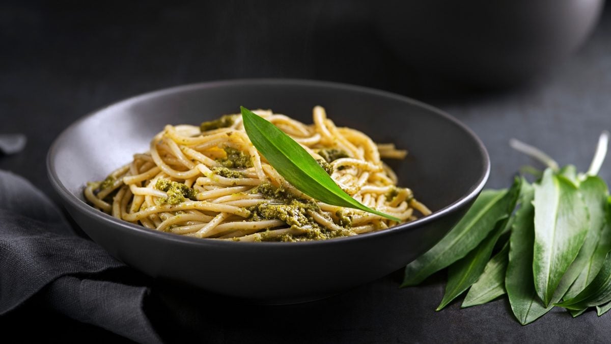 Eine schwarze Schale mit dem Pastagericht von der Seite auf dunklem Tisch mit frischem Bärlauch fotografiert.