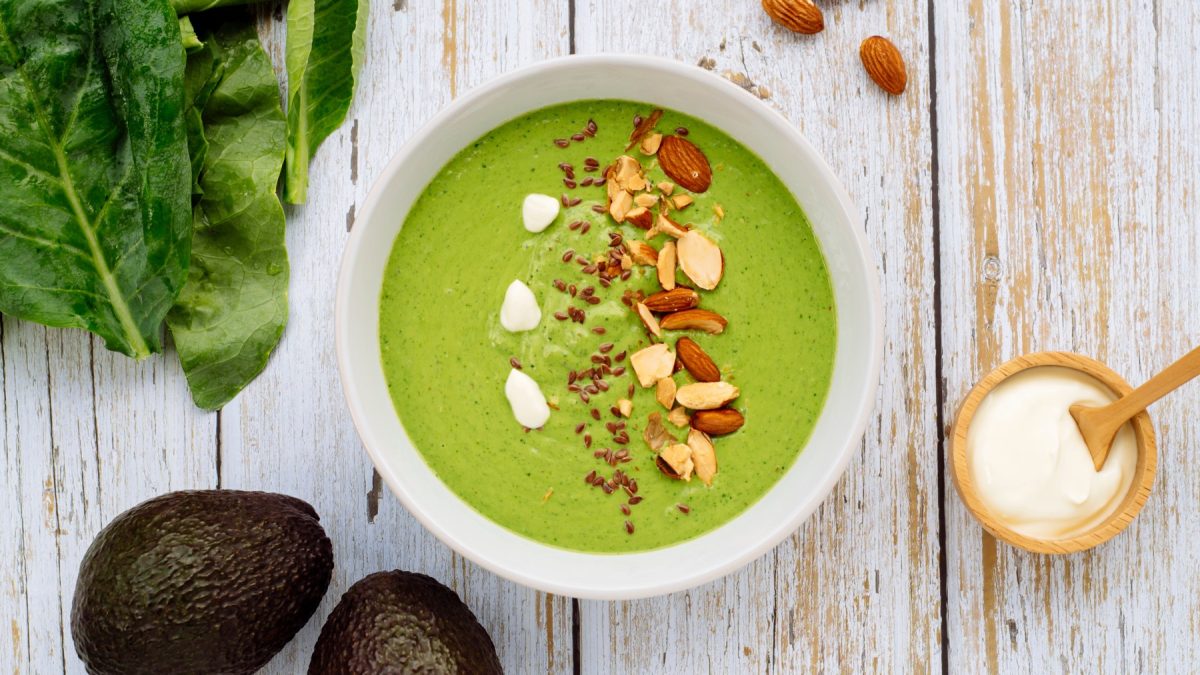 Spargel-Smoothie-Bowl in einer weißen Schüssel auf weißem Hintergrund. Links unten Avocado, links oben Spinat.
