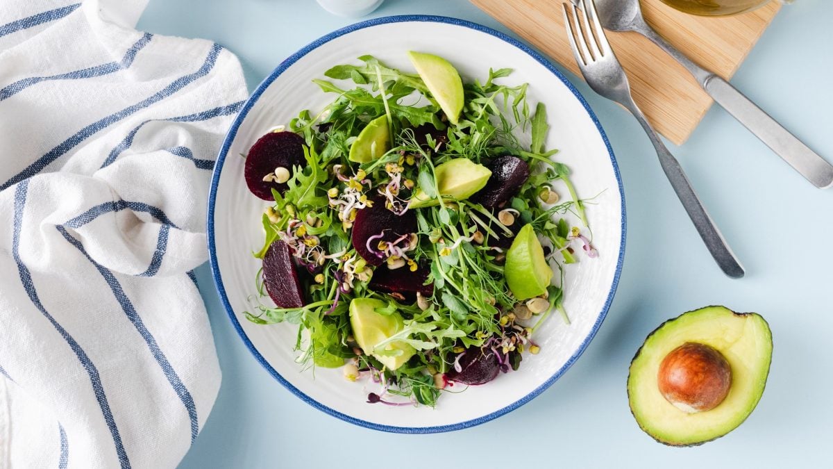 Sprossensalat mit Roter Bete und Avocado auf einem hellen Teller. Daneben eine angeschnittene Avocado mit Kern.