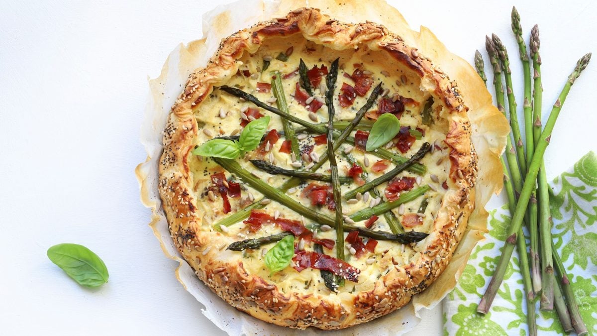 Torta salata auf weißem Untergrund mit grünem Spargel daneben.