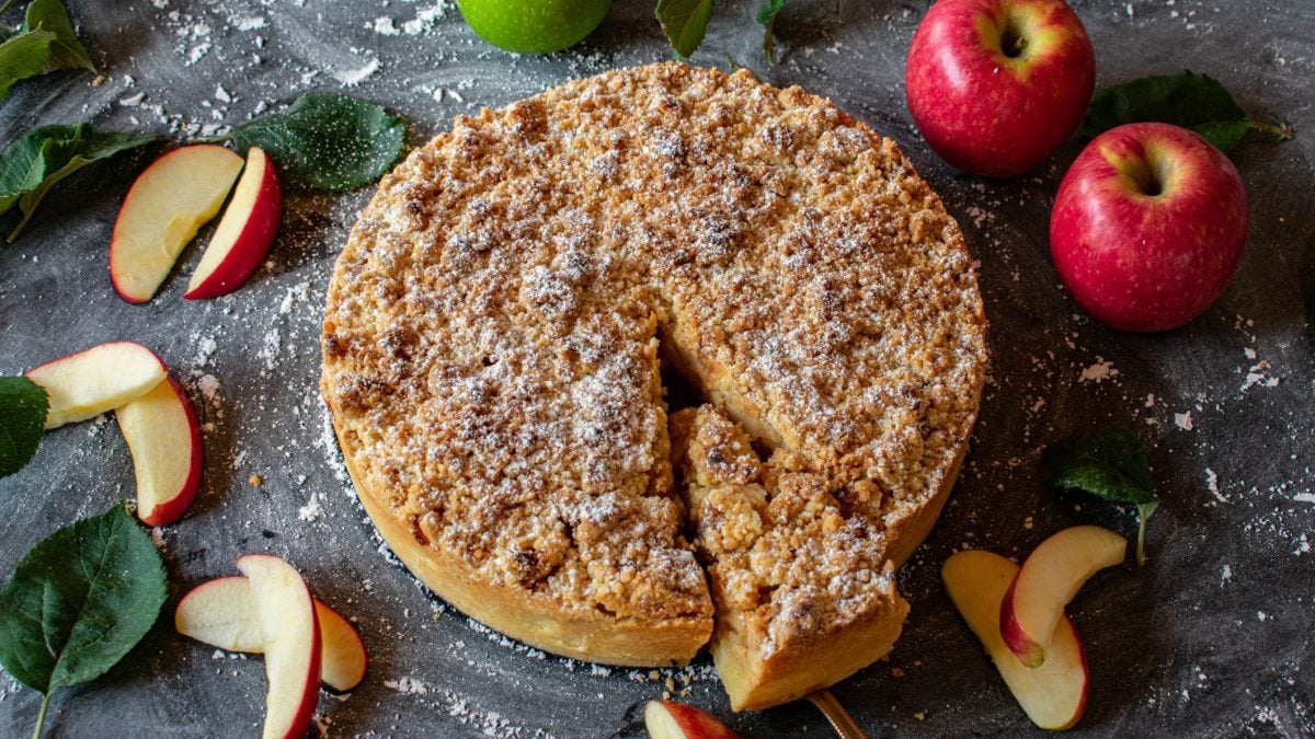 Angeschnittener Apfel-Streuselkuchen von oben fotografiert, daneben frische Äpfel.