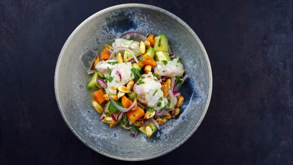 Ein hellblauer Teller, mit dem Ceviche direkt von oben auf einem dunkelblauen Untergrund serviert.