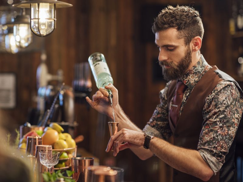 Ein Barkeeper steht am Tresen einer professionellen Bar und mixt gerade einen Cocktail.