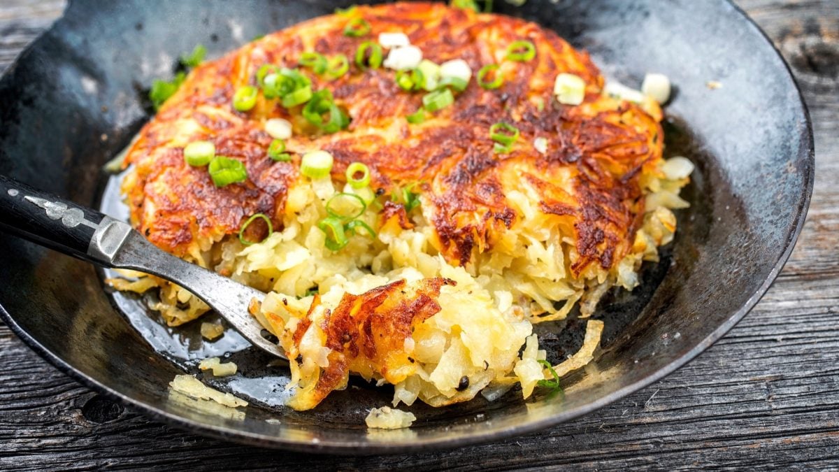 Draufsicht schräg: Eine schwarze gusseiseren Pfanne mit knusprig gebratenen Berner Rösti.