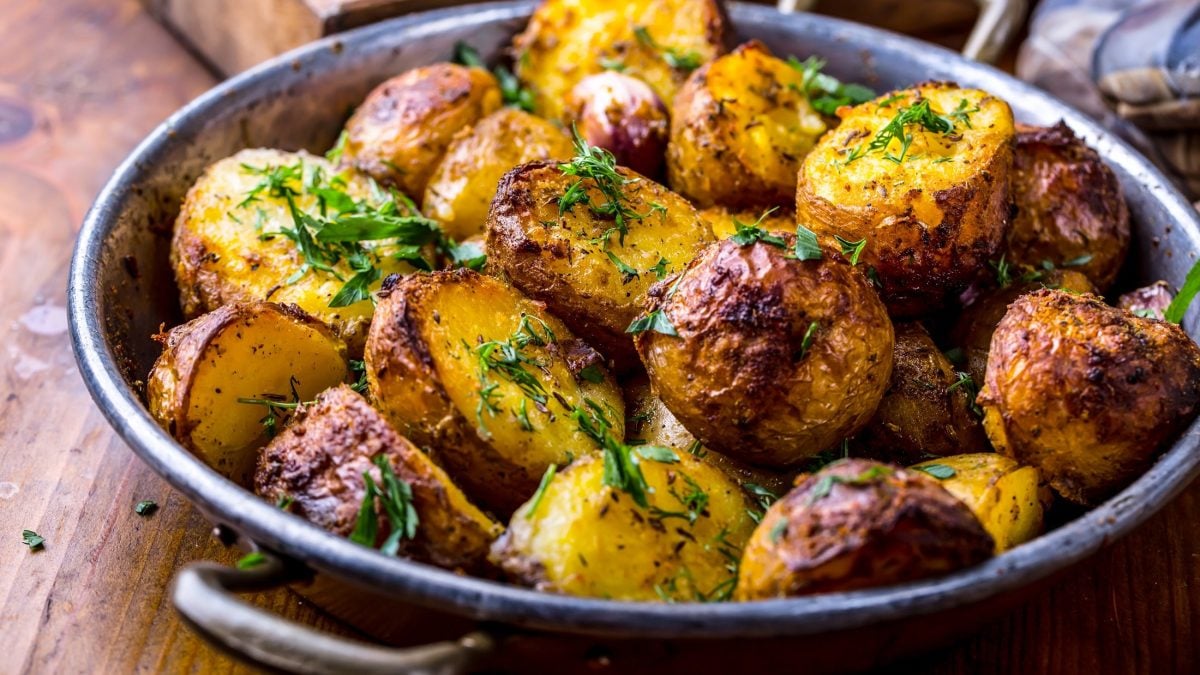 Draufsicht, schräg: gebratene Dill-Kartoffeln aus der Bratpfanne auf einem rustikalen Untergrund aus Holz.