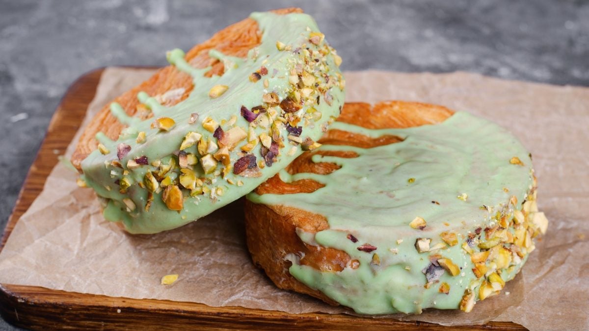 Draufsicht, schräg: Zwei New York Rolls mit Pistaziencreme liegen auf einem Holzbrettchen.