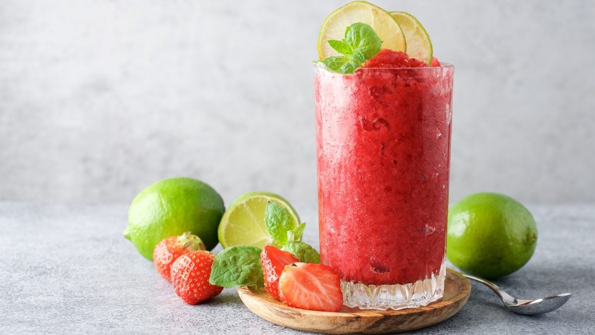 Erdbeerlimes-Granita in einem hohen Glas, dekoriert mit frischen Limetten und Minze.