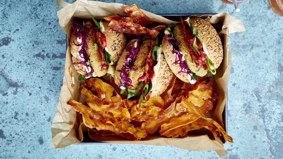 Draufsicht: Falafel Bacon Burger mit Süßkartoffelchips in viereckiger Form auf blauem Untergrund.