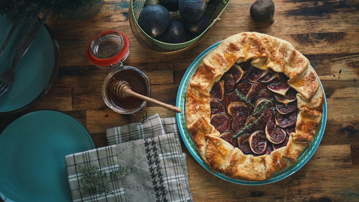 Hausgemachte Feigengalette auf Holztisch, garniert mit Thymian, neben Honig und türkisfarbenen Tellern.