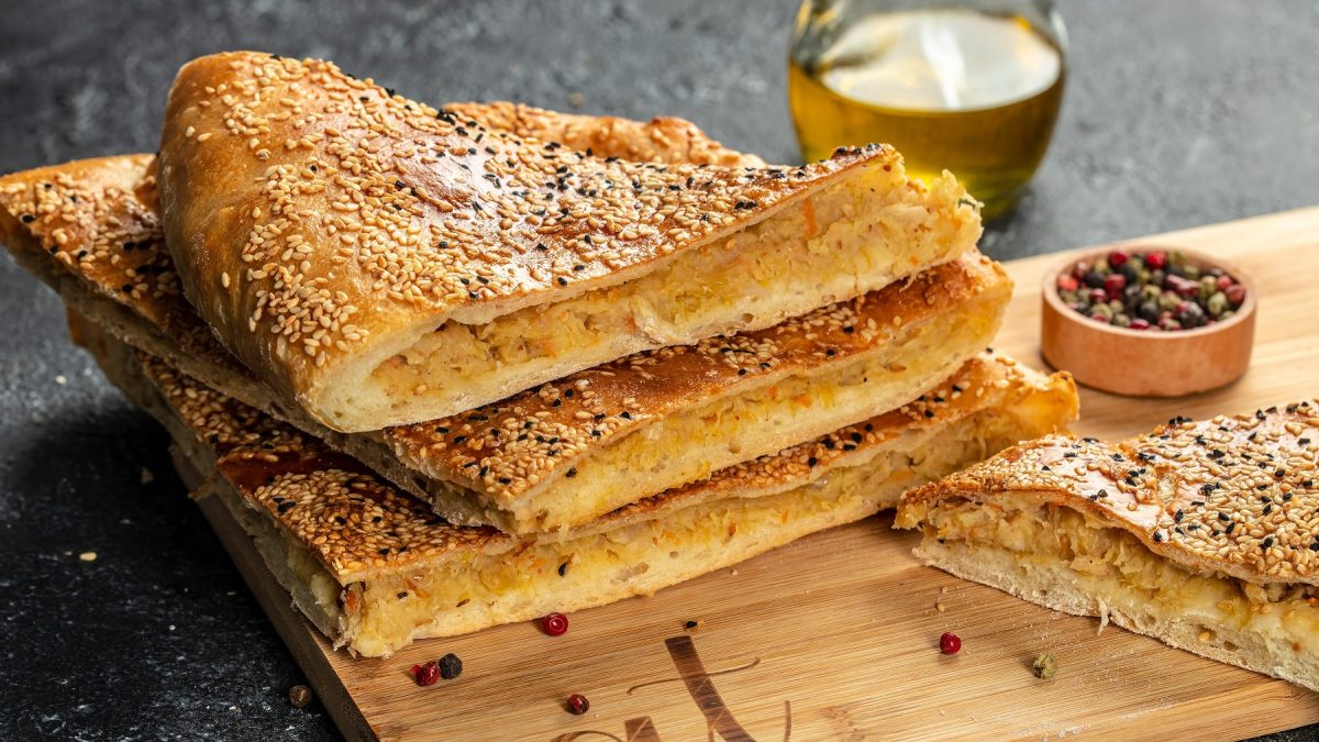 Gefüllte Fladenbrot übereinander gestapelt auf einem Holzbrett. Daneben eine Schale mit Gewürzen.