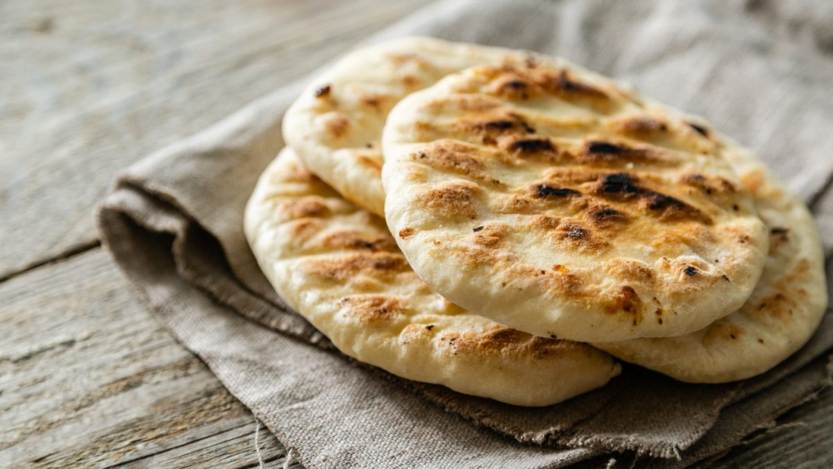 Glutenfreies Pita-Brot auf einem beigen Geschirrtuch auf braunem Hintergrund.
